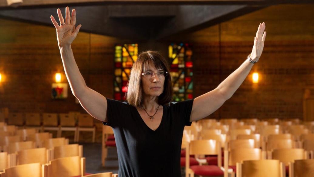 Frau betet mit offenen Armen in einer Kirche