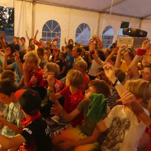 Viele Kinder sitzen in einem Zelt und heben ihre Hände.