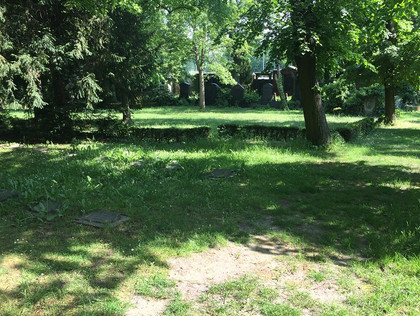Auf dem Bild ist ein grüne Wiese, Bäume un dein paar Grabplatten zu sehen. Das Foto zeigt einen Teil eines Friedhofs in Berlin. 