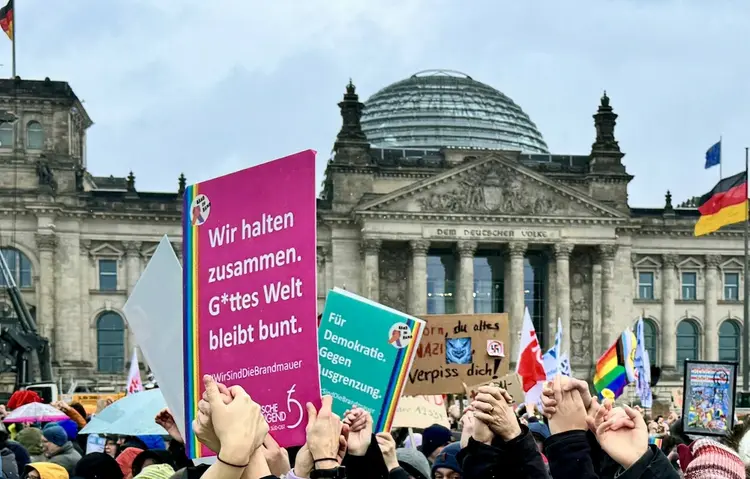Menschen, die sich vor dem Reichstag zum Protestieren versammelt haben und Plakate für den Schutz der Demokratie in die Luft halten.