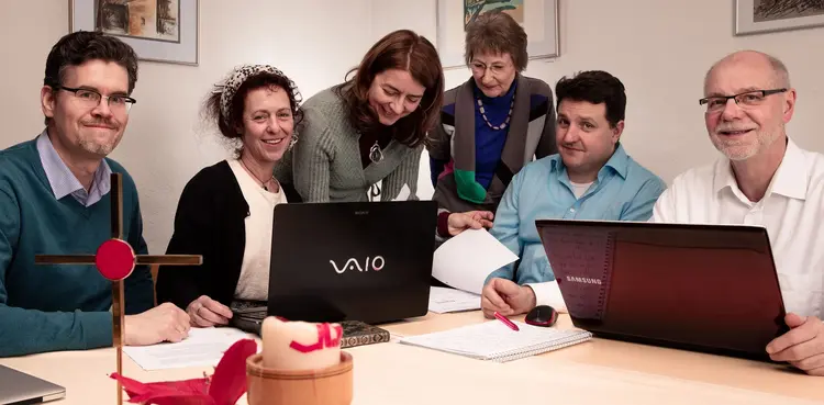 Sechs Personen des Gemeindekirchenrats sitzen an einem Tisch vor Stift und Papier und Laptops.