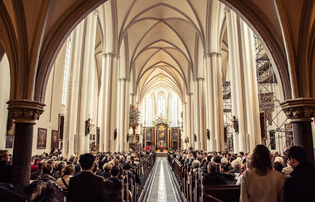 Der Weg zum Altar ist lang, zu sehen ist die gefüllte Kirche, der rote Teppich, der zwischen den Bänken zum Altar führt und Menschen von hinten und im Hintergrund der Altar, Foto: Matthias Kauffmann