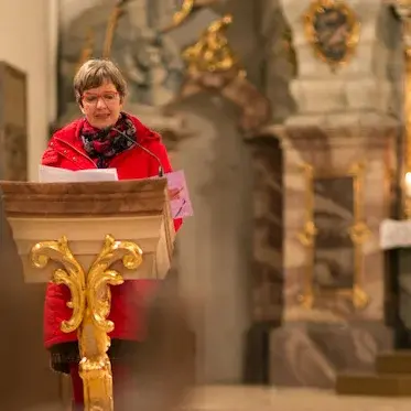 Blick zum Altar in einer Kirche. Links ein Lesepult mit Lektorin in roter Jacke