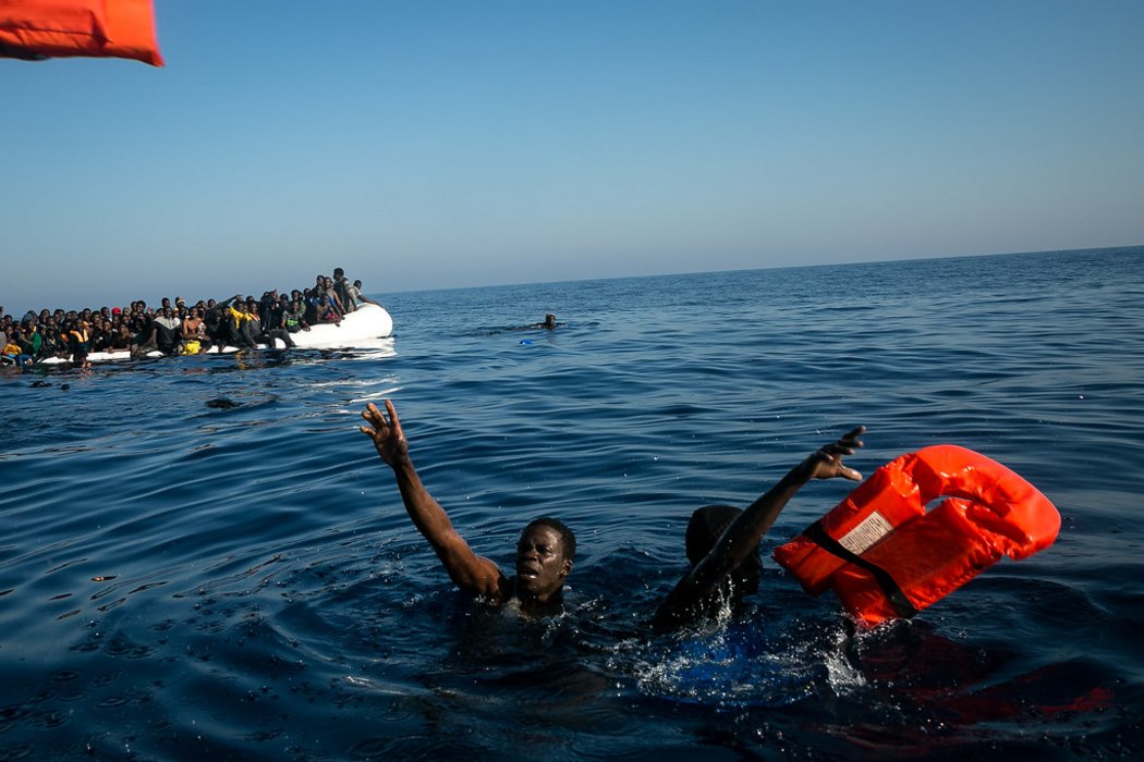 Geflüchtete Menschen im offenen Meer, denen Rettungswesten zugeworfen werden.