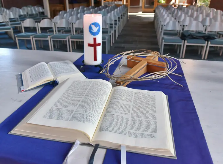 Auf einem Altar liegen aufgeklappt eine Bibel und ein Gesangsbuch, zudem ein Holzkreuz, eine Kerze und ein Weidenring/Dornenkrone.