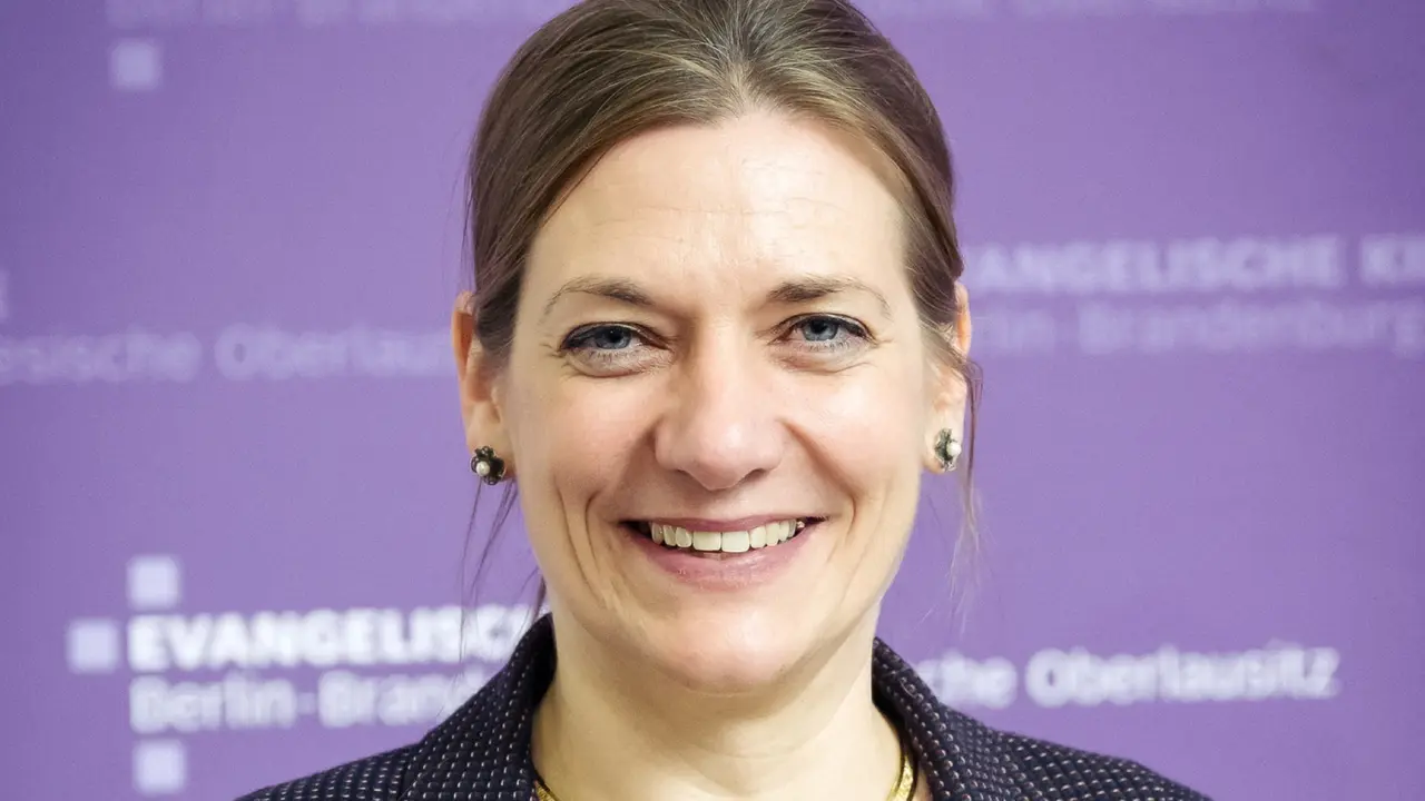 Portrait der Konsistorialpräsidentin Dr. Viola Vogel vor violettem Hintergrund, auf dem das EKBO Zeichen zu sehen ist.