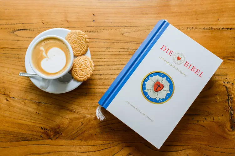 Auf einem Tisch die Luther Bibel und ein Tasse Kaffee mit Keksen, in Form der Lutherrose.