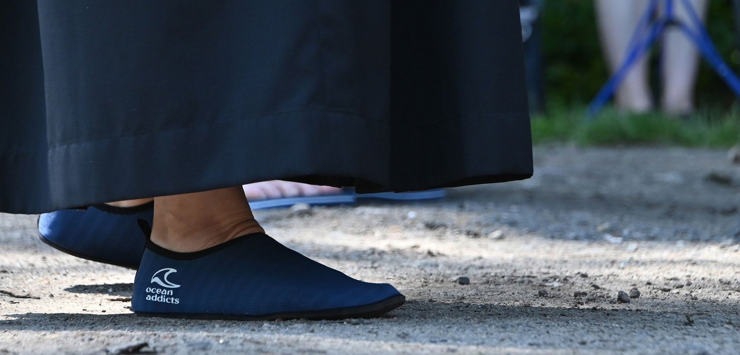 Füße einer Pfarrerin, die Badeschuhe trägt, auf denen ,,ocean addicts'' und das Zeichen einer Welle stehen.
