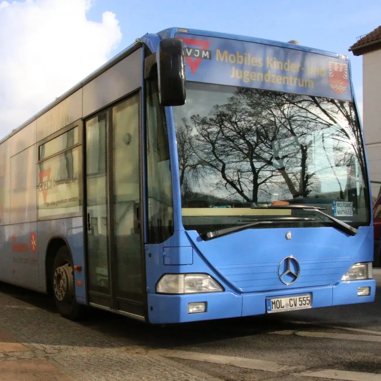 Ein blauer Bus steht auf einer Straße. Über der Windschutzscheibe steht die Aufschrift ,,mobiles Kinder- und Jugendzentrum''.