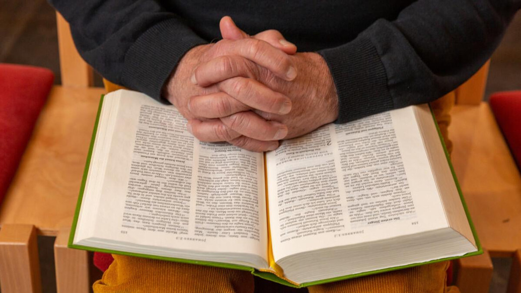 Zum Gebet gefaltete Hände, auf eine offene Bibel gelegt