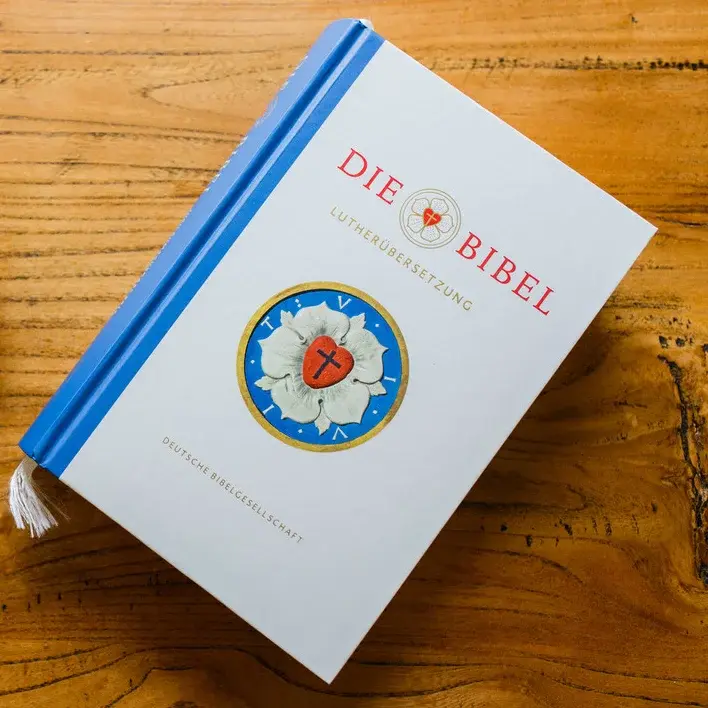 Auf einem Tisch die Luther Bibel und ein Tasse Kaffee mit Keksen, in Form der Lutherrose.