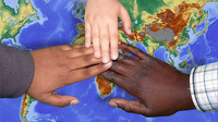 drei Hände, eine "weiße", eine dunkelhäutige, eine "schwarze" berühren sich über der Weltkarte