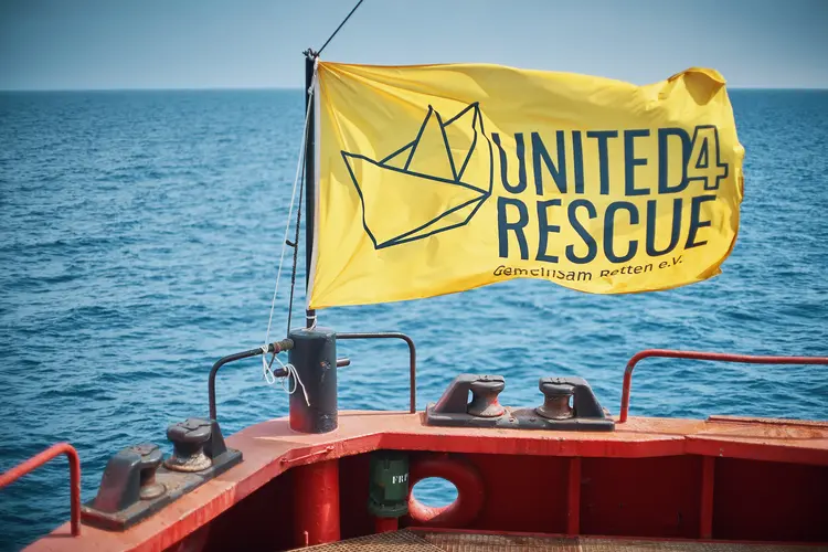 Eine am Boot befestigte gelbe Fahne mit der Aufschrift ,,United for Rescue''. Im Hintergrund das Meer.