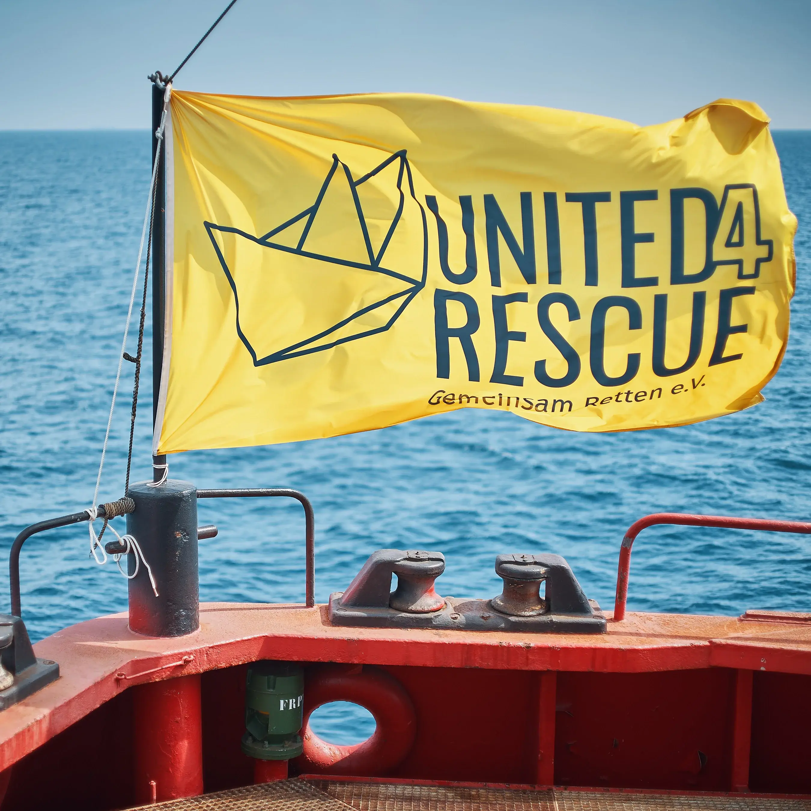 Eine am Boot befestigte gelbe Fahne mit der Aufschrift ,,United for Rescue''. Im Hintergrund das Meer.