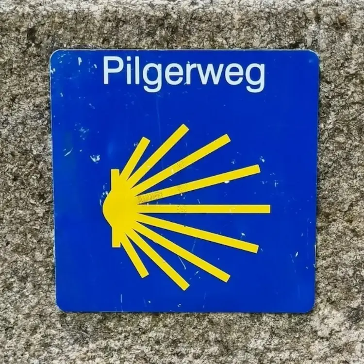 Das blau-gelbe Pilgerwegschild auf einem Stein. 