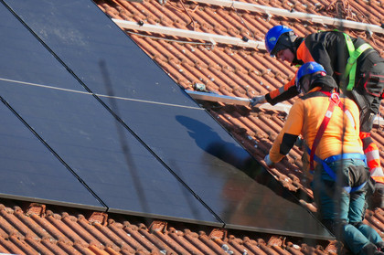 Zwei Handwerker installieren eine Solaranlage auf einem Hausdach.