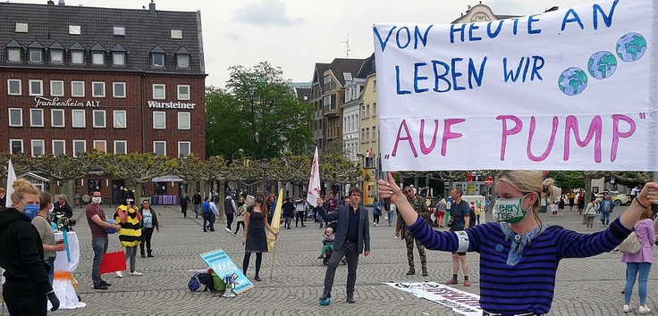 Menschen demonstrieren auf einem Platz in Düsseldorf. Auf einem Plakat steht "Von heute an leben wir auf Pump"