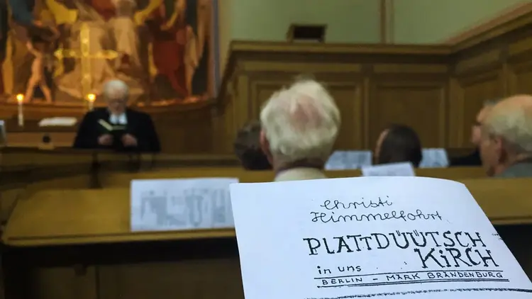 Personen sitzen auf Kirchenbänken bei einem Himmelfahrts-Gottesdienst auf plattdeutsch.