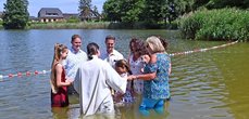Sieben Personen stehen in einem Kreis im See und halten sich an den Händen. In ihrer Mitte stehen Kinder.