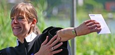 Eine Pfarrerin streckt ihren Arm zur Seite raus und zeigt auf ihn. Auf dem Unterarm stehen geschriebene Worte, unter anderem das Wort ,,Segen''.