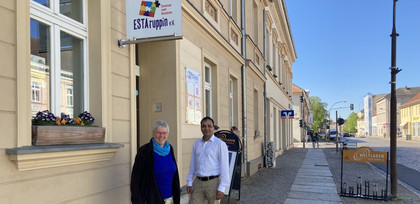 Links ist das ESTA-haus der Vielfalt in Neuruppin zu sehen, vor der Eingangstür stehen Pfarrerin Christiane Schulz, Geschäftsführerin von ESTAruppin e. V. und ESTAruppin-Mitarbeiter Ferdydun Rahimi in der Bildmitte.