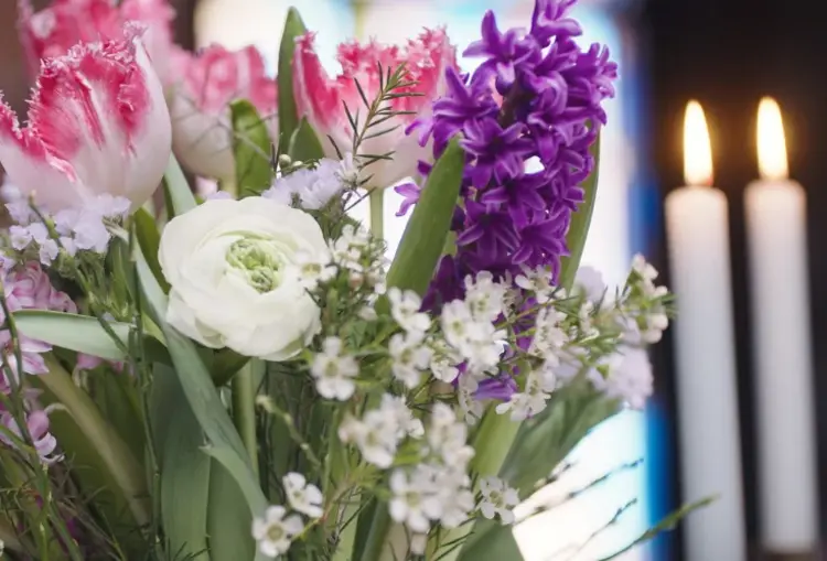 Blumenstrauß mit weißen, violetten und rosa farbenen Blumen. Im Hintergrund stehen zwei angezündete Kerzen.