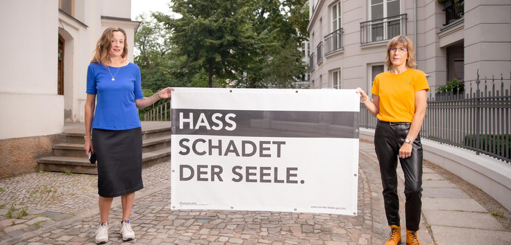 Zwei Frauen halten ein Plakat "Hass schadet der Seele".