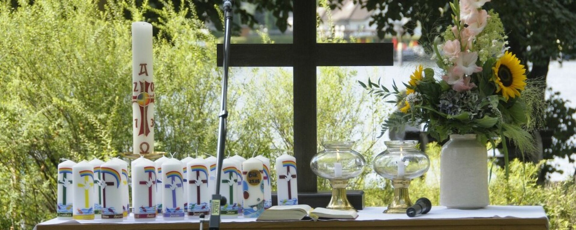 Ein Altar am See, auf dem Kerzen, Blumen und ein Kreuz stehen.