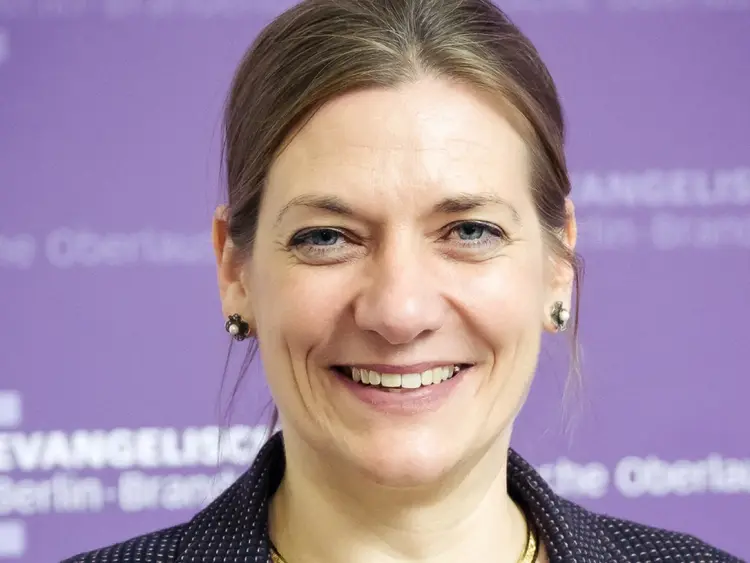 Portrait der Konsistorialpräsidentin Dr. Viola Vogel vor violettem Hintergrund, auf dem das EKBO Zeichen zu sehen ist.