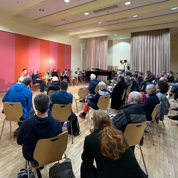 Mehrere Personen sitzen in einem Raum auf Stühlen und nehmen an dem Popmusik Symposium namens Sympop teil.
