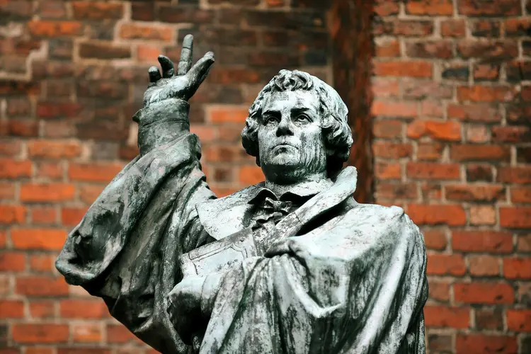 Statue von Martin Luther mit erhobener Hand vor einer Kirche.