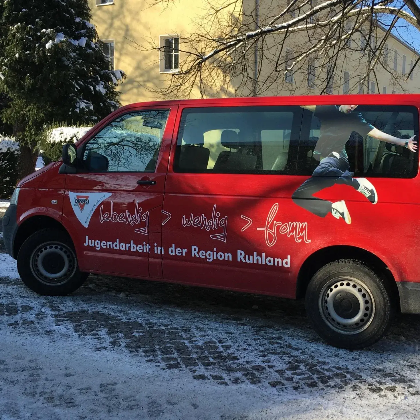 Ein roter Kleinbus mit der Aufschrift ,,Jugendarbeit in der Region Ruhland'' steht auf einer Straße.