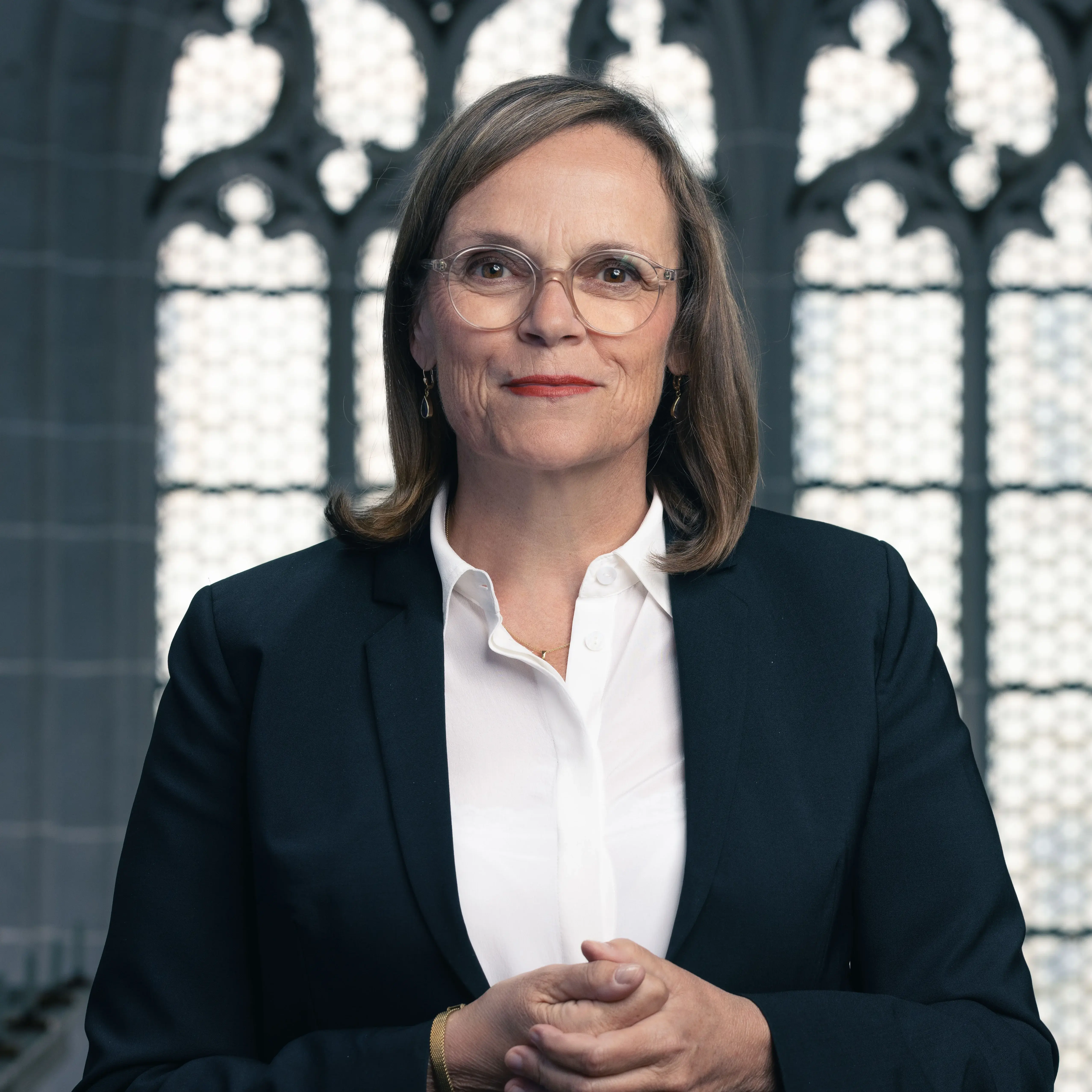 Portrait von Theresa Rinecker in weißer Bluse und schwarzem Blazer. Im Hintergrund ein Kirchenfenster.