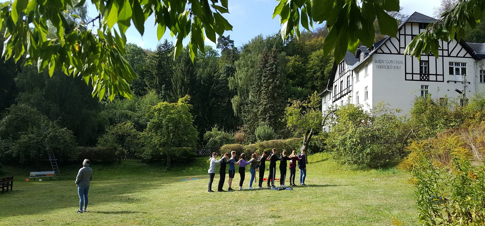 Gäste- und Tagungshaus Die Malche, eine Gruppe übt im Garten Vertrauen, Jugendliche legen einander die Hände auf die Schultern und teilen Schrit für Schritt den Weg, Foto: Gundula Eichler